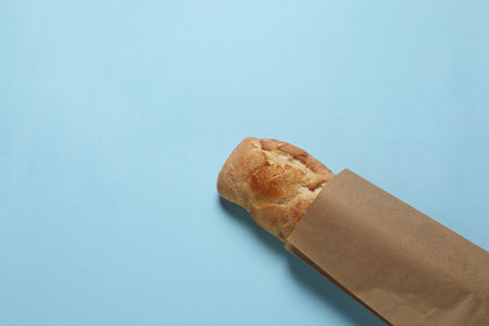 Paper bag with fresh baguette on light blue background, top view. Space for textの写真素材