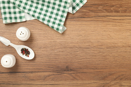 Checkered tablecloth and spices on wooden table, flat lay. Space for text