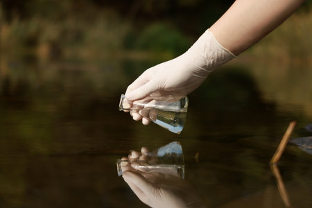 Examination of water quality. Researcher taking water sample from lake outdoors, closeupの写真素材