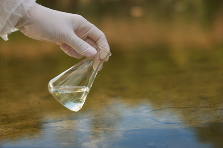 Examination of water quality. Researcher holding flask with sample from lake outdoors, closeup.の写真素材