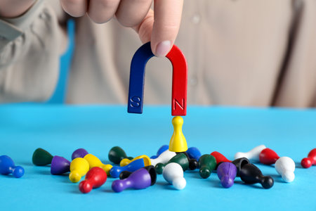 Woman with magnet attracting yellow piece among colorful ones on light blue background, closeup