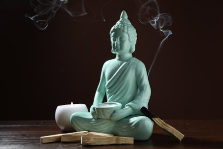 Smoldering palo santo stick, burning candles and Buddha statue on wooden table against dark background, closeupの写真素材