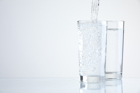 Pouring refreshing soda water into glasses on light background, closeup. Space for textの写真素材