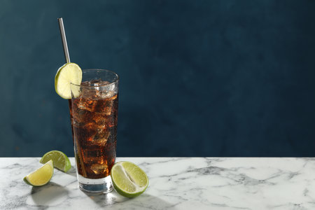 Refreshing iced cola with lime slices on white marble table against blue background. Space for text