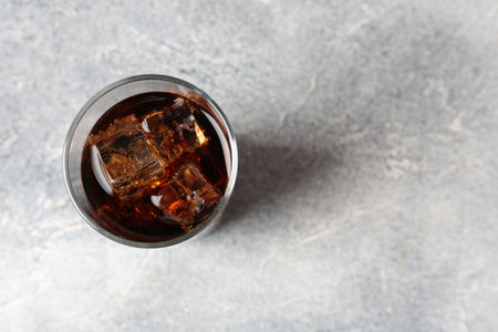 Refreshing cola with ice cubes in glass on light textured table, top view. Space for text