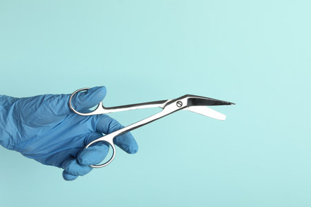 Doctor with surgical scissors on turquoise background, closeup. Space for text