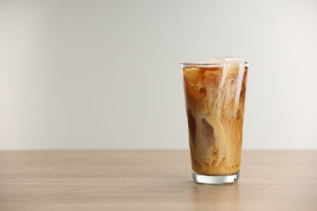 Refreshing iced coffee with milk in glass on wooden table against light background. Space for textの写真素材