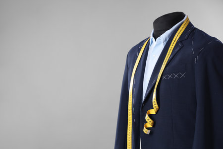 Semi-ready jacket, shirt and measuring tape on mannequin against gray background, closeup. Space for textの写真素材