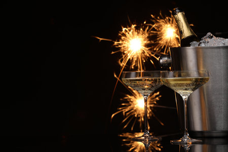 Glasses of sparkling wine with sparklers and bottle in cooler bucket on black background. Space for textの写真素材