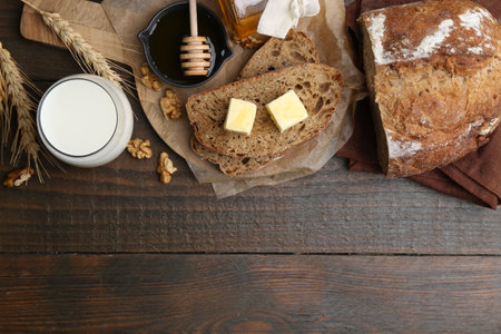 Slices of bread with butter, honey, milk and walnuts on wooden table, flat lay. Space for text