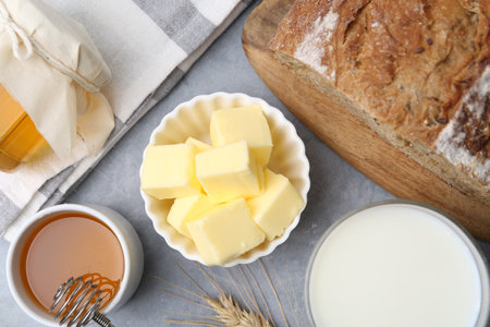 Fresh butter, milk, honey and bread on gray table, flat layの写真素材