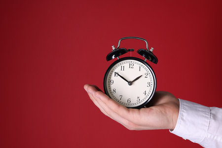 Man with alarm clock on red background, closeup. Space for textの写真素材