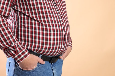 Overweight man in tight shirt on beige background, closeup. Space for textの写真素材