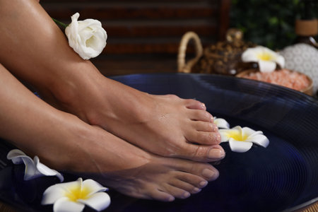 Woman soaking her feet in bowl with water and plumeria flowers on floor, closeup. Spa treatmentの写真素材