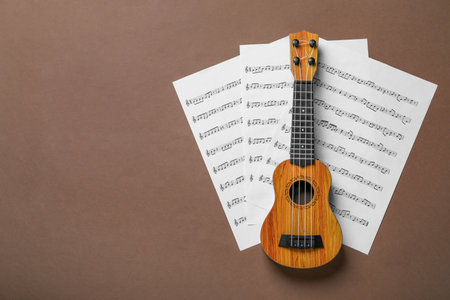Ukulele and music sheets on brown background, top view. Space for textの写真素材