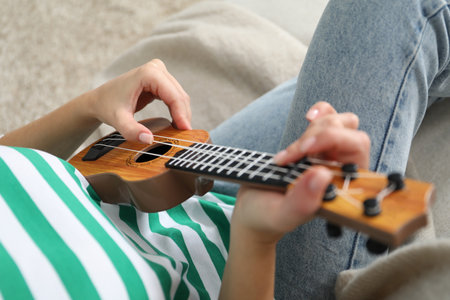 Woman playing ukulele on sofa at home, closeup