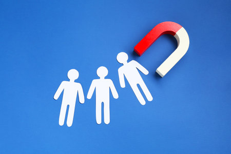 Magnet attracting paper human figures on blue background, flat layの写真素材