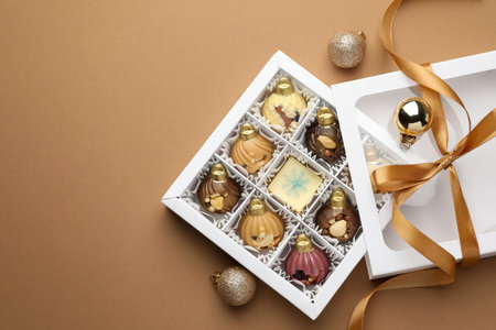 Delicious chocolate in shape of ornaments in open box and Christmas decor on beige background, flat lay. Space for textの写真素材
