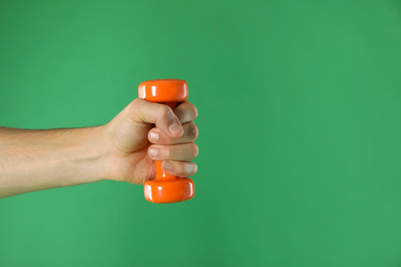 Man exercising with dumbbell on green background, closeup. Space for textの写真素材