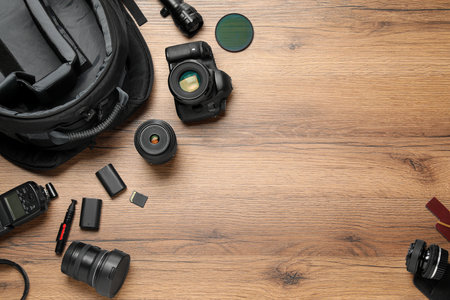 Professional photographer's equipment and backpack on wooden background, flat lay. Space for text