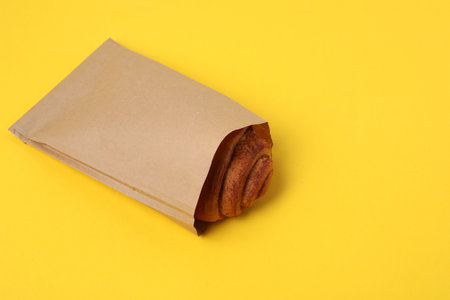 Paper bag with freshly baked bun on yellow background. Space for textの写真素材