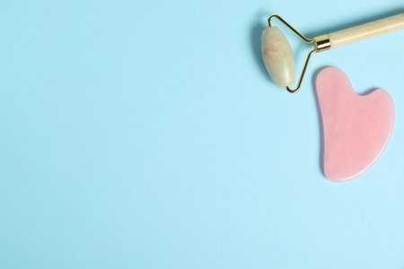 Face roller and gua sha tool on light blue background, top view. Space for textの写真素材