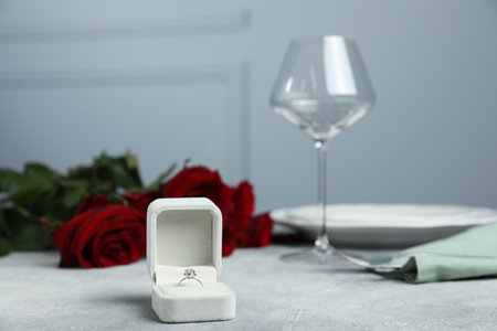 Beautiful setting for romantic dinner, engagement ring and roses on light table