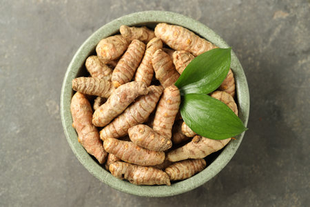 Tumeric rhizomes with leaves in bowl on gray table, top view