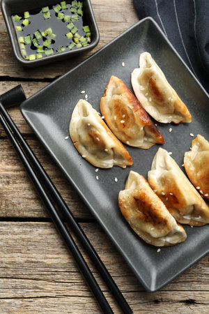 Delicious fried gyoza dumplings with sesame seeds served on wooden table, flat lay