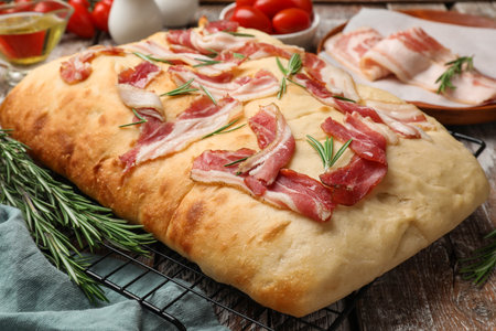 Delicious focaccia bread with bacon, rosemary, oil and tomatoes on wooden table, closeupの写真素材