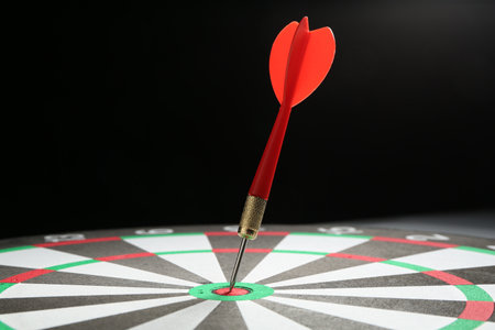 Red arrow hitting target on dart board against black background, closeupの写真素材
