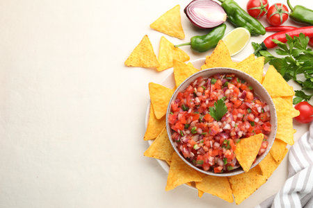 Delicious salsa in bowl, ingredients and nacho chips on beige table, flat lay. Space for textの写真素材