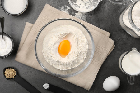 Baking powder with egg yolk in bowl surrounded by other products on gray textured table, flat layの写真素材