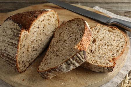 Cut loaf of fresh bread and knife on wooden table, closeup