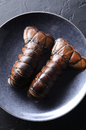 Raw lobster tails on black table, top view