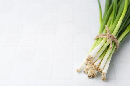 Bunch of fresh green onions on white tiled table. Space for text