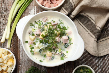 Delicious okroshka soup in bowl and ingredients on wooden table, flat layの写真素材