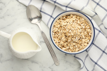 Tasty oatmeal in bowl and milk served on white marble table, flat layの写真素材