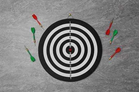 Dart board and colorful arrows on gray marble background, flat lay