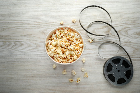 Tasty popcorn and film reel on white wooden background, flat layの写真素材