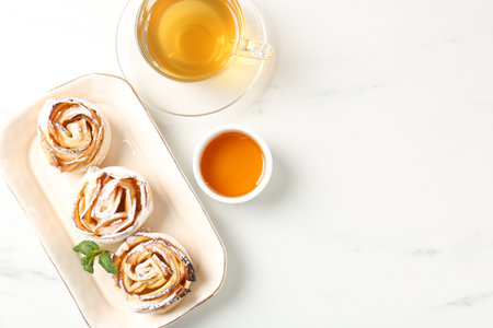 Freshly baked apple roses with mint, honey and tea on white marble table, flat lay. Space for textの写真素材