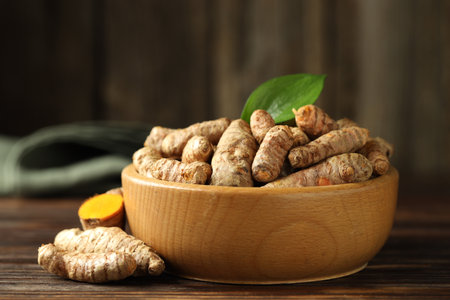 Tumeric rhizomes with leaf in bowl on wooden table, closeup