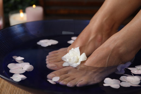 Woman soaking her feet in bowl with water and flowers on floor, closeup. Spa treatmentの写真素材