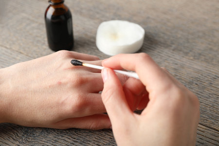 Woman applying topical liquid with cotton swab on hand at wooden table, closeupの写真素材