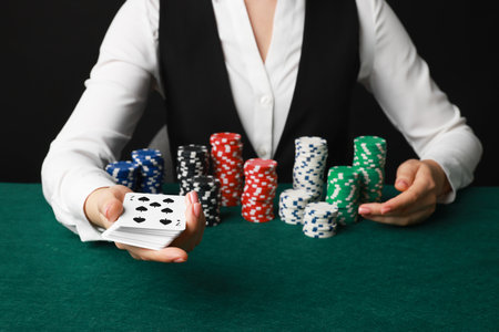 Professional croupier with casino chips and playing cards at gambling table on black background, closeupの写真素材