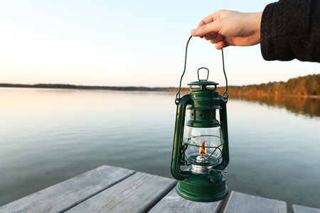 Man with vintage kerosene lamp near river in evening, closeup. Space for textの写真素材