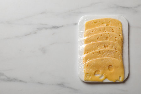 Pack of sliced cheese on white marble table, top view. Space for text