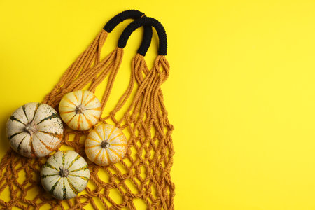 Macrame shopping bag and pumpkins on yellow background, top view. Space for textの写真素材