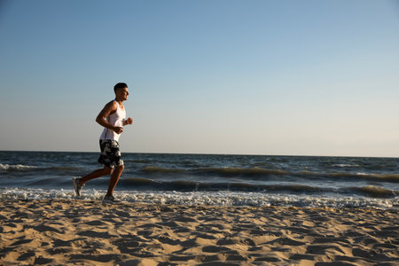 Sporty man running on sandy beach at sunset