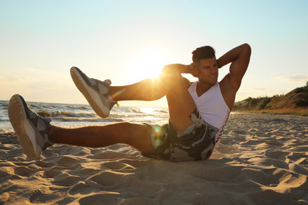 Sporty man with athletic body doing crunches on beachの写真素材